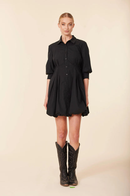 Woman wearing a black dress and cowboy boots on a beige background