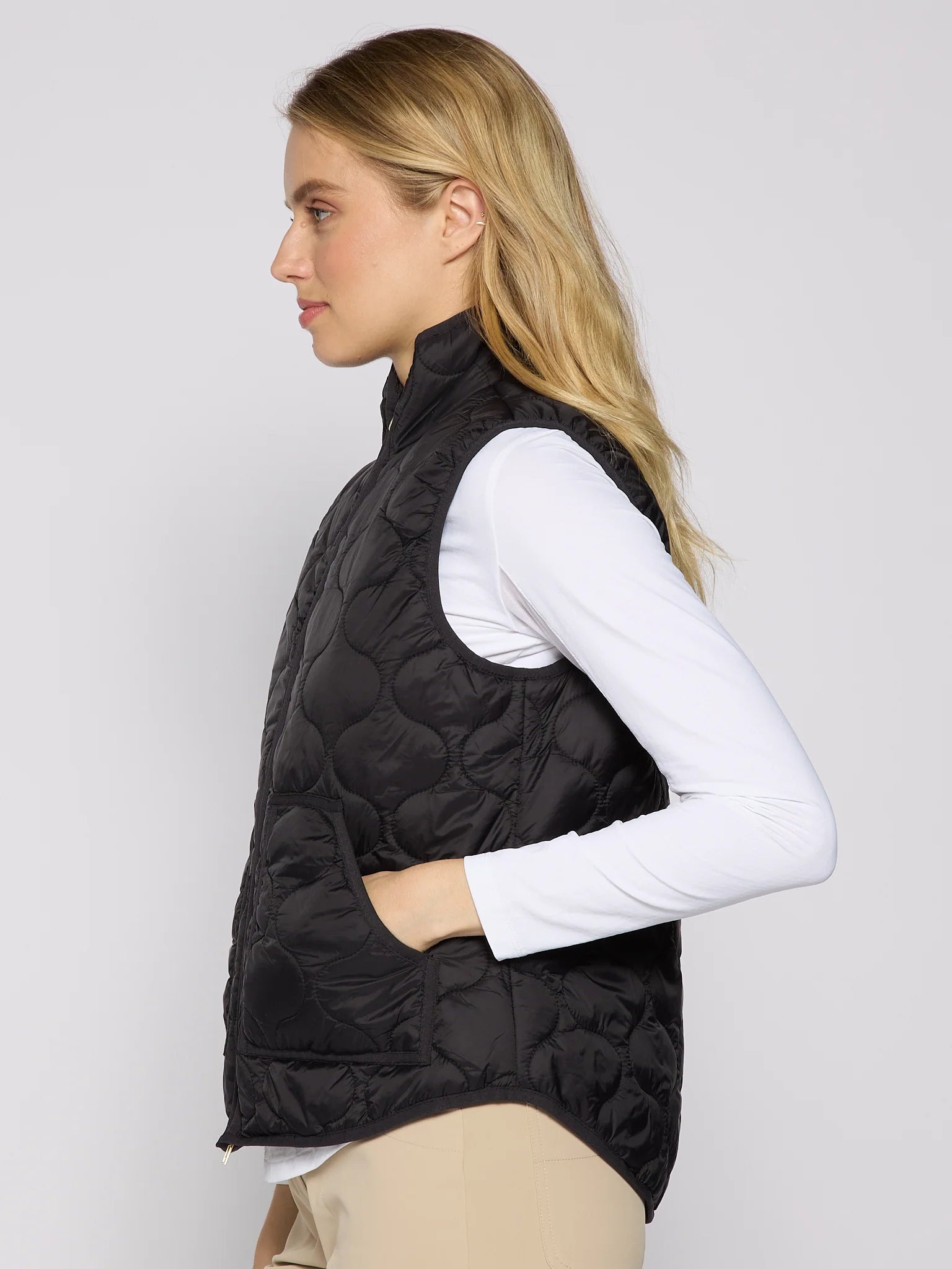 Woman wearing a black quilted vest over a white long-sleeve shirt on a plain background