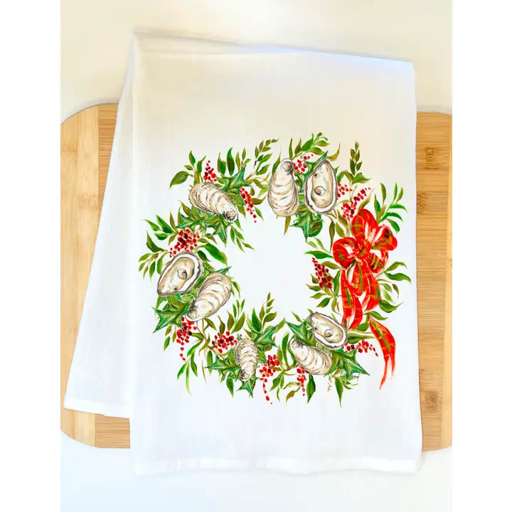 White towel with a decorative wreath design featuring oysters, greenery, and a red bow on a wooden surface.