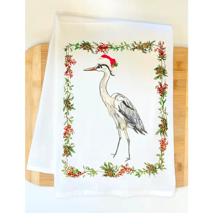 Towel with a heron wearing a Santa hat and surrounded by Christmas wreath on a wooden surface.