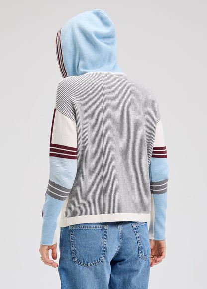 Backside of a person wearing a gray sweater with colorful sleeves and blue jeans on a light gray background