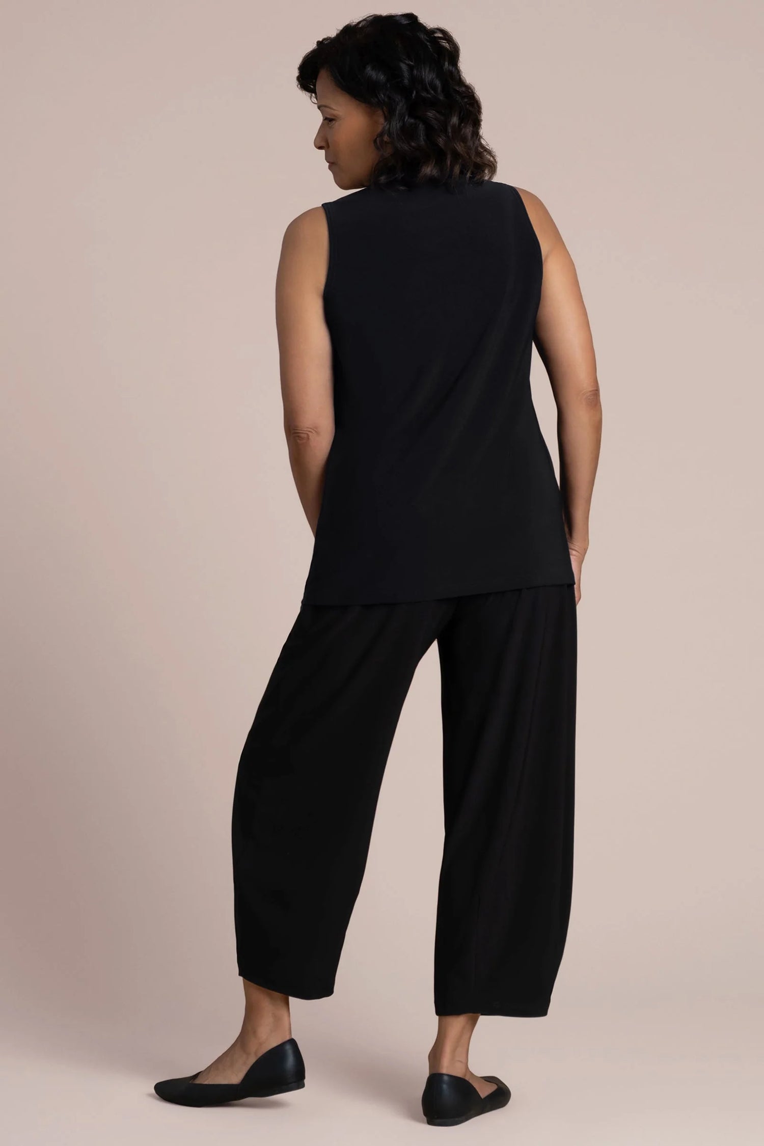 A woman wearing a sleeveless black V-neck top and black pants by Sympli Deep V Trapeze Tank