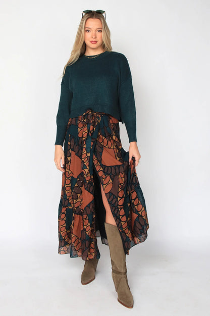 Woman wearing a green sweater and patterned skirt with brown boots on a white background