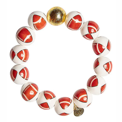 A beaded stretch bracelet featuring 14 white and red football-shaped beads, one gold metallic ball, and a small gold charm.
