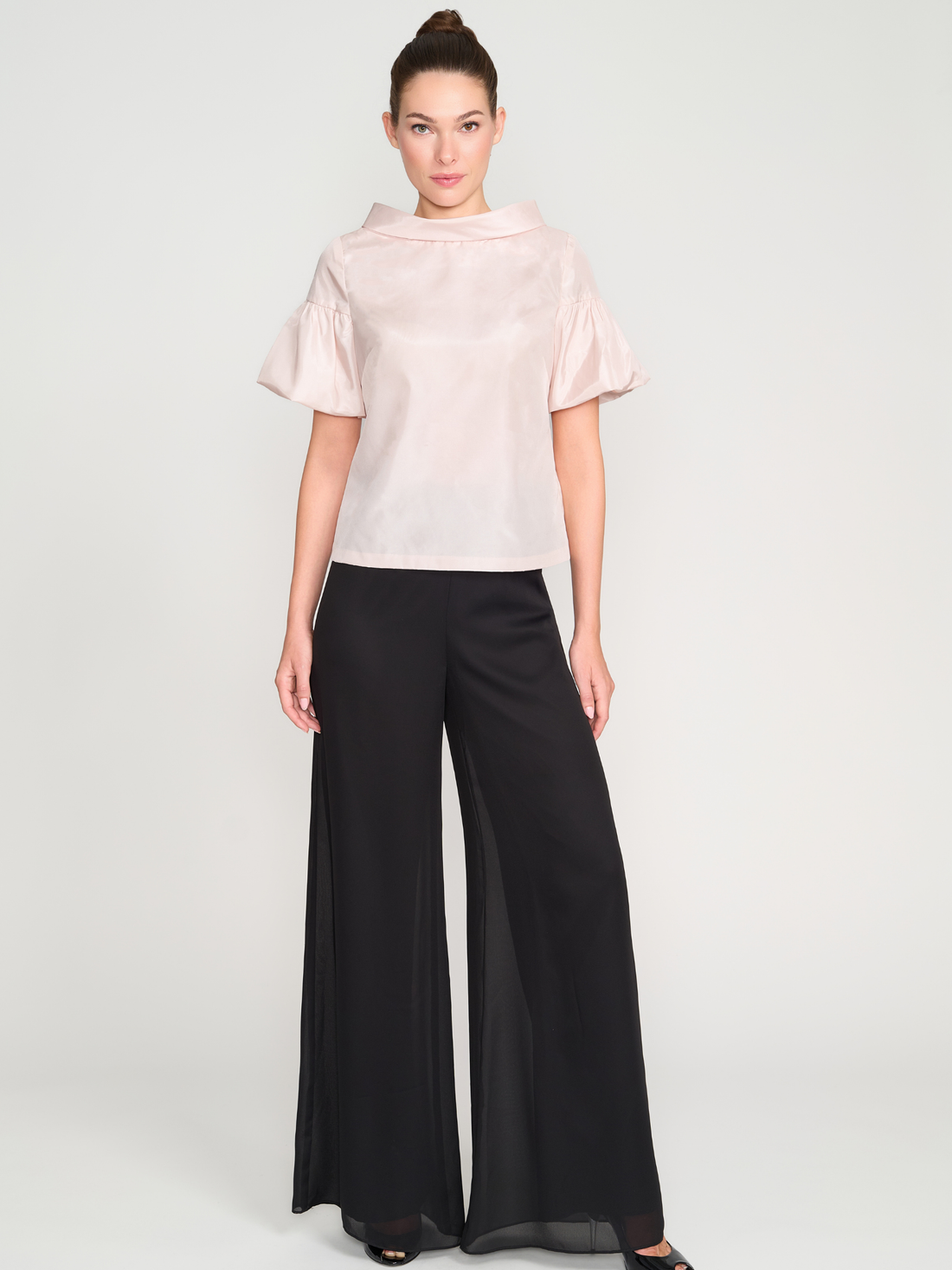 Woman wearing a light pink blouse and black wide-leg pants on a white background