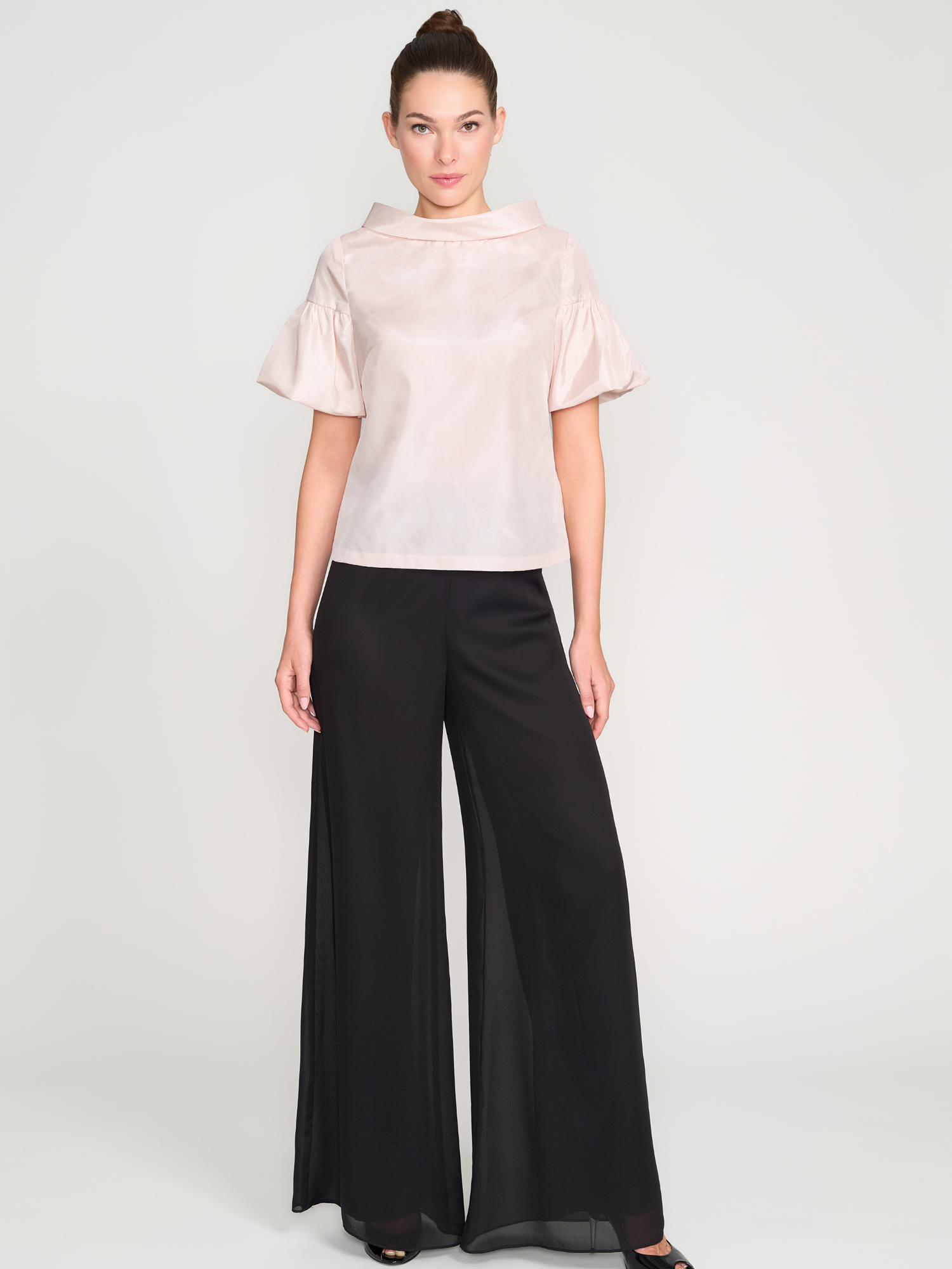 Woman wearing a light pink blouse and black wide-leg pants on a white background