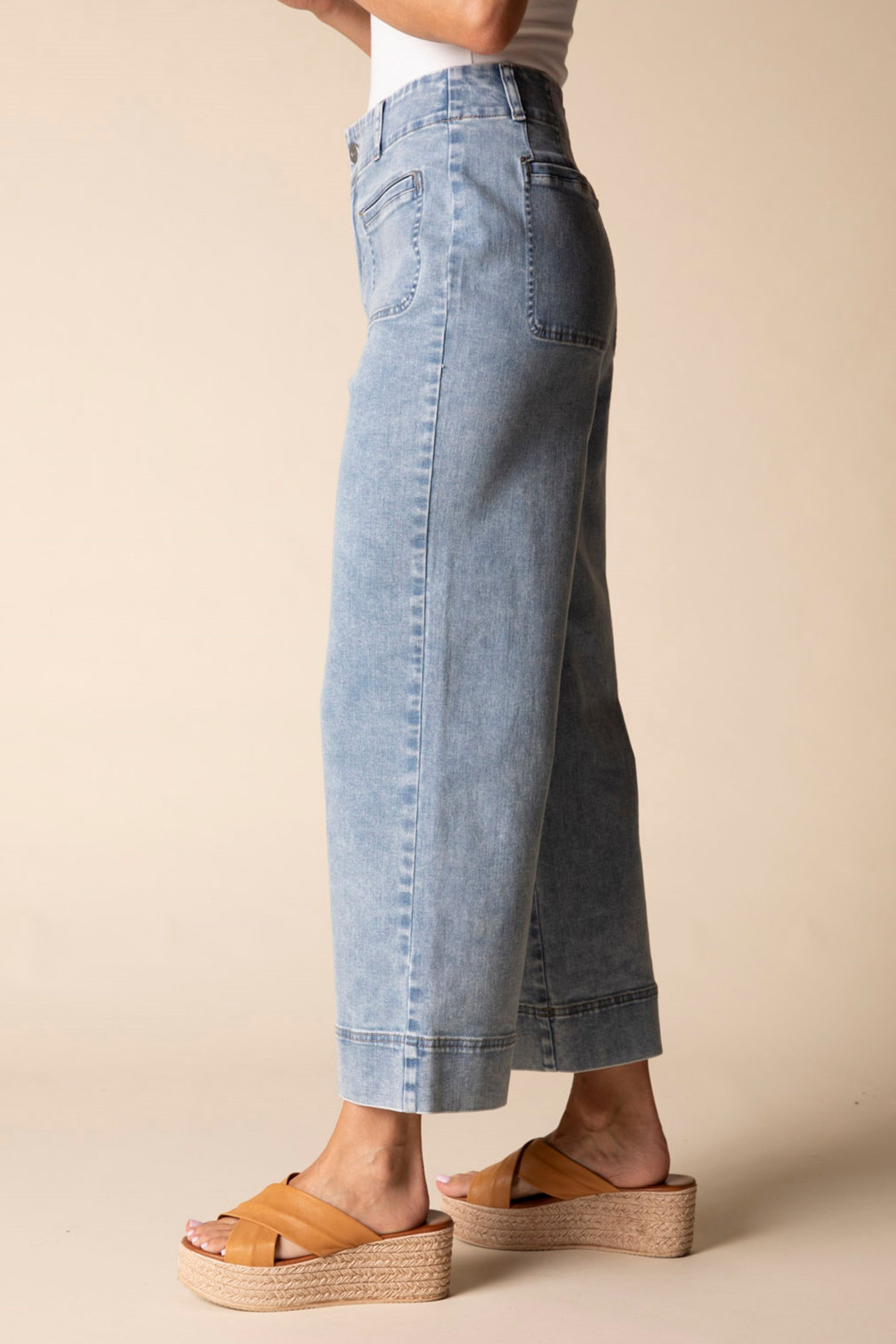 Person wearing light blue denim jeans on a beige background