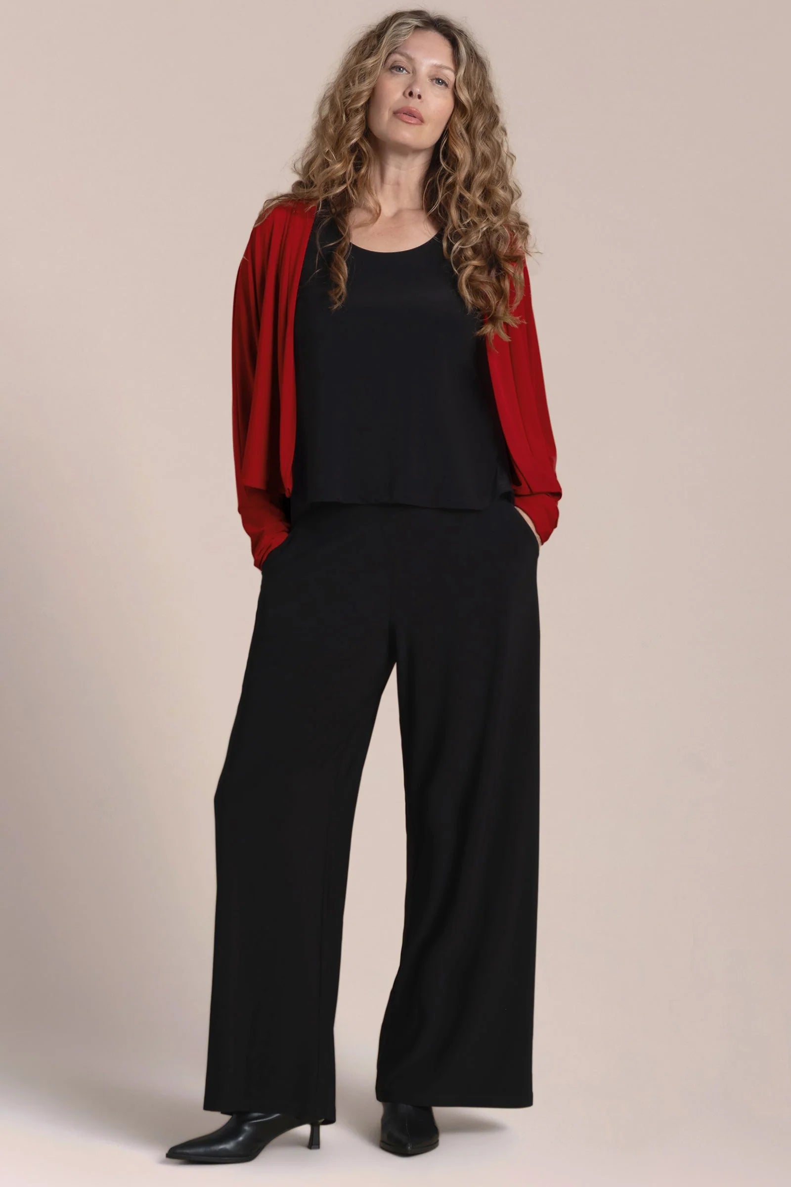 Woman wearing a red jacket, black top, and black pants against a beige background