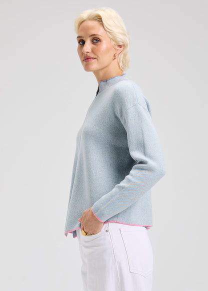 Woman wearing a light blue sweater with dark blue and pink details with a plain background