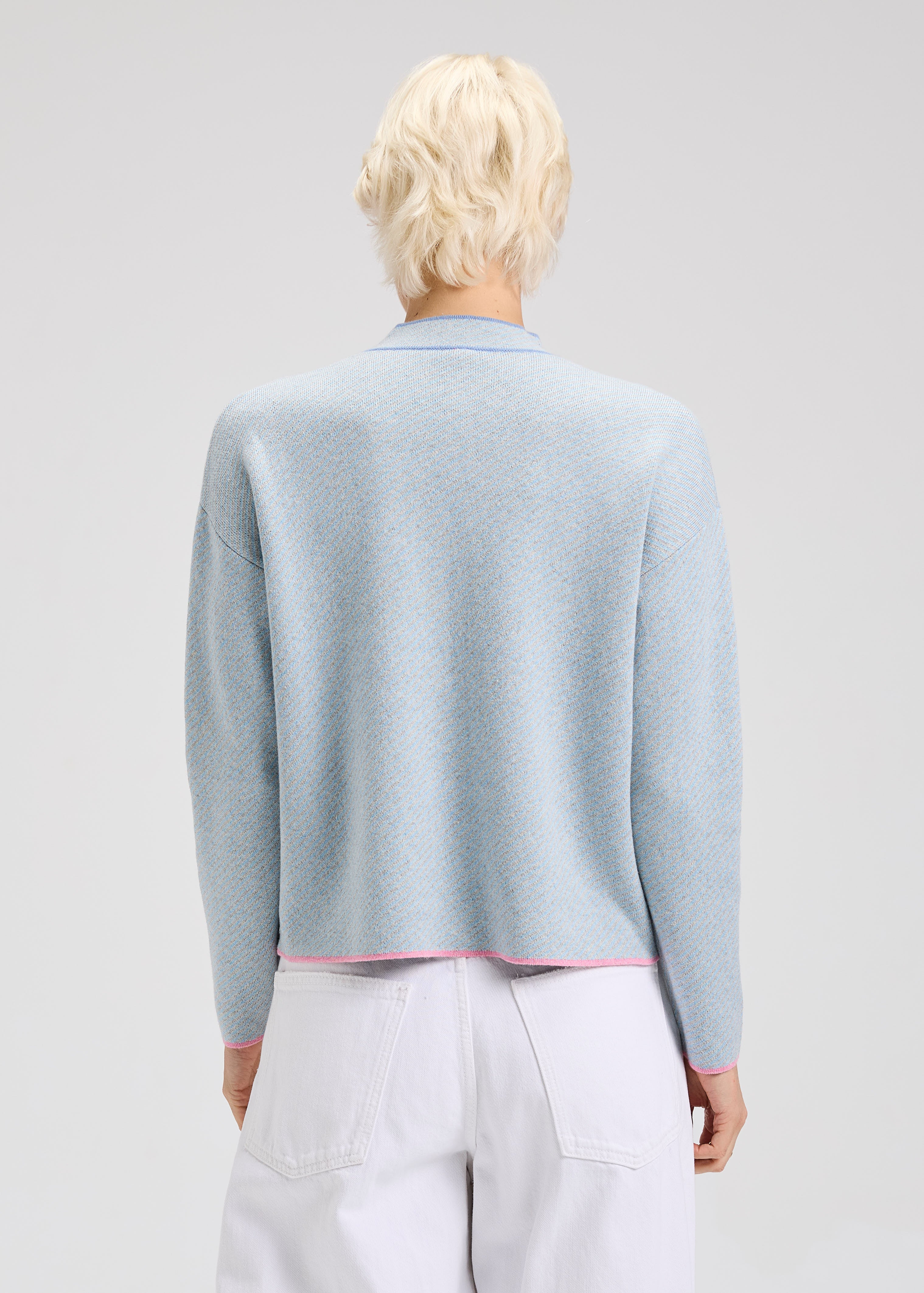 Person wearing a light blue sweater with dark blue and pink details with a plain background