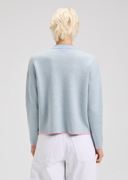 Person wearing a light blue sweater with dark blue and pink details with a plain background