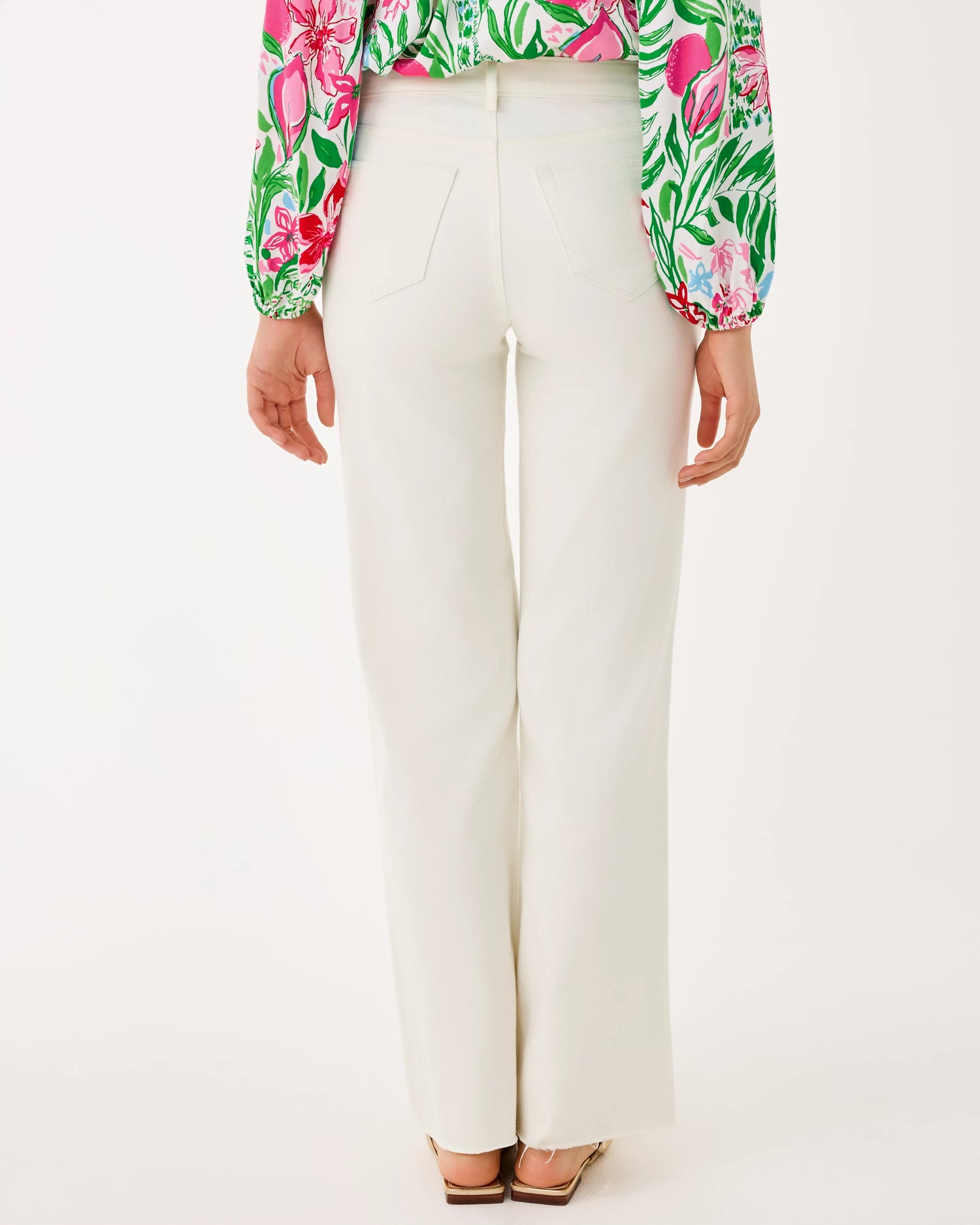 Person wearing a colorful floral blouse and white pants on a white background