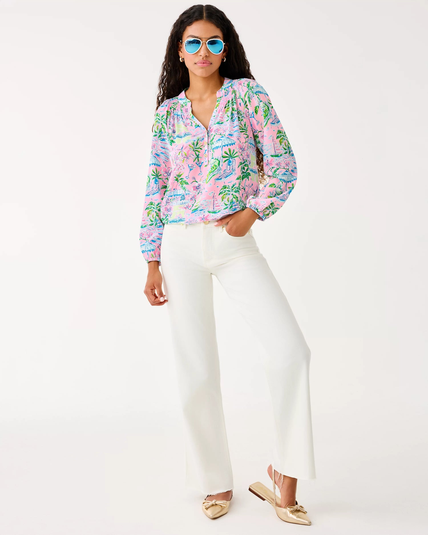 Woman wearing a colorful floral blouse and white pants on a white background