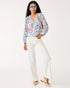Woman wearing a colorful floral blouse and white pants on a white background
