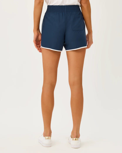 A model wearing navy blue athletic shorts with white piping trim lilly pulitzer UPF 50+ Luxletic 4" Backcourt Short color low tide navy
