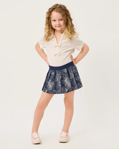 A young girl lilly pulitzer girls sylvana skort  Low Tide Navy Lil Palm Prowl navy blue pleated skirt with a white botanical pattern 