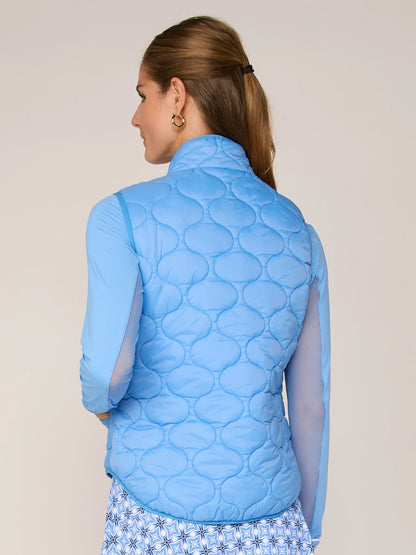Woman wearing a blue quilted vest against a beige background