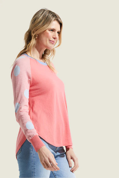 Woman wearing a pink long-sleeve top with patterned sleeves on a beige background