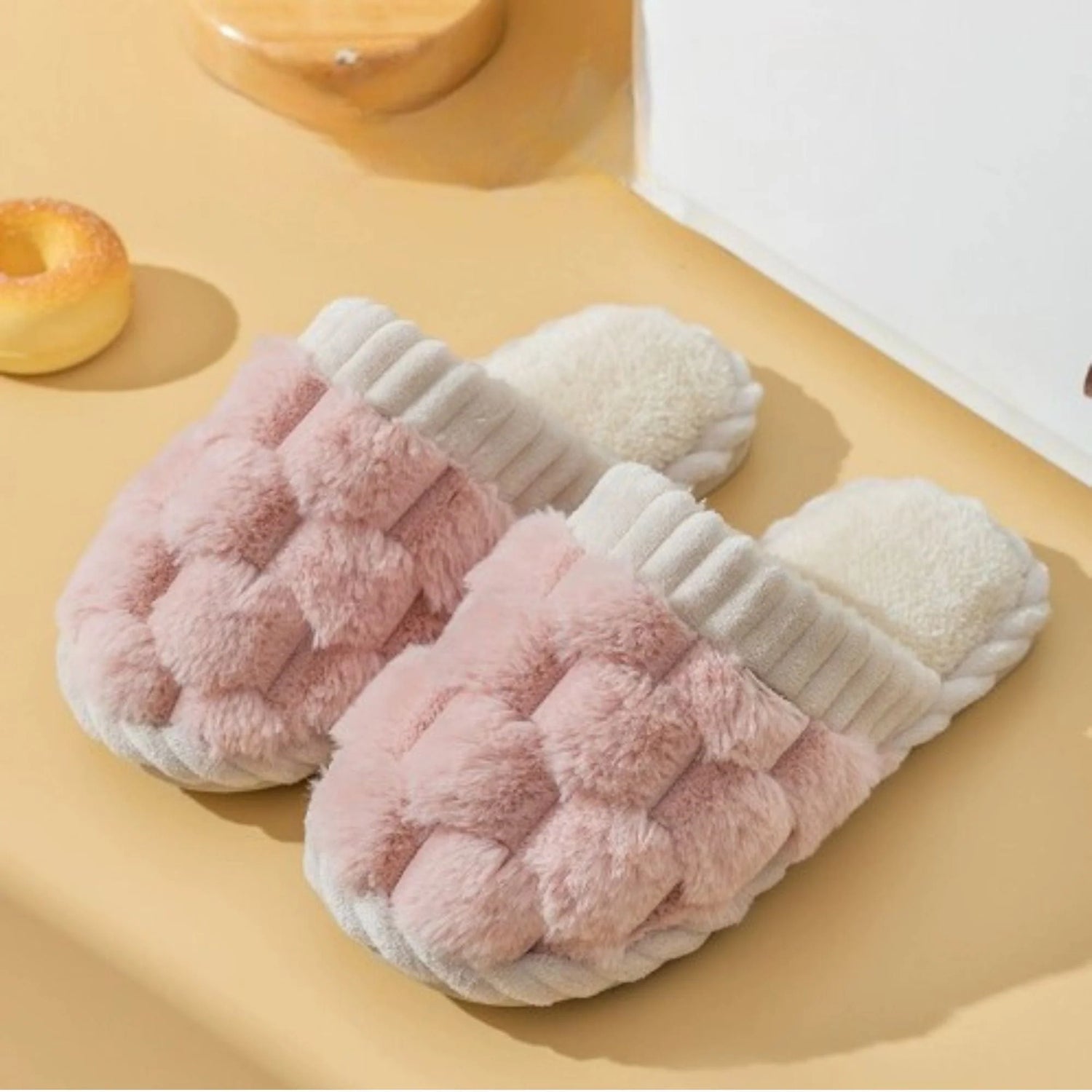 Pair of pink and white fuzzy slippers on a beige surface.