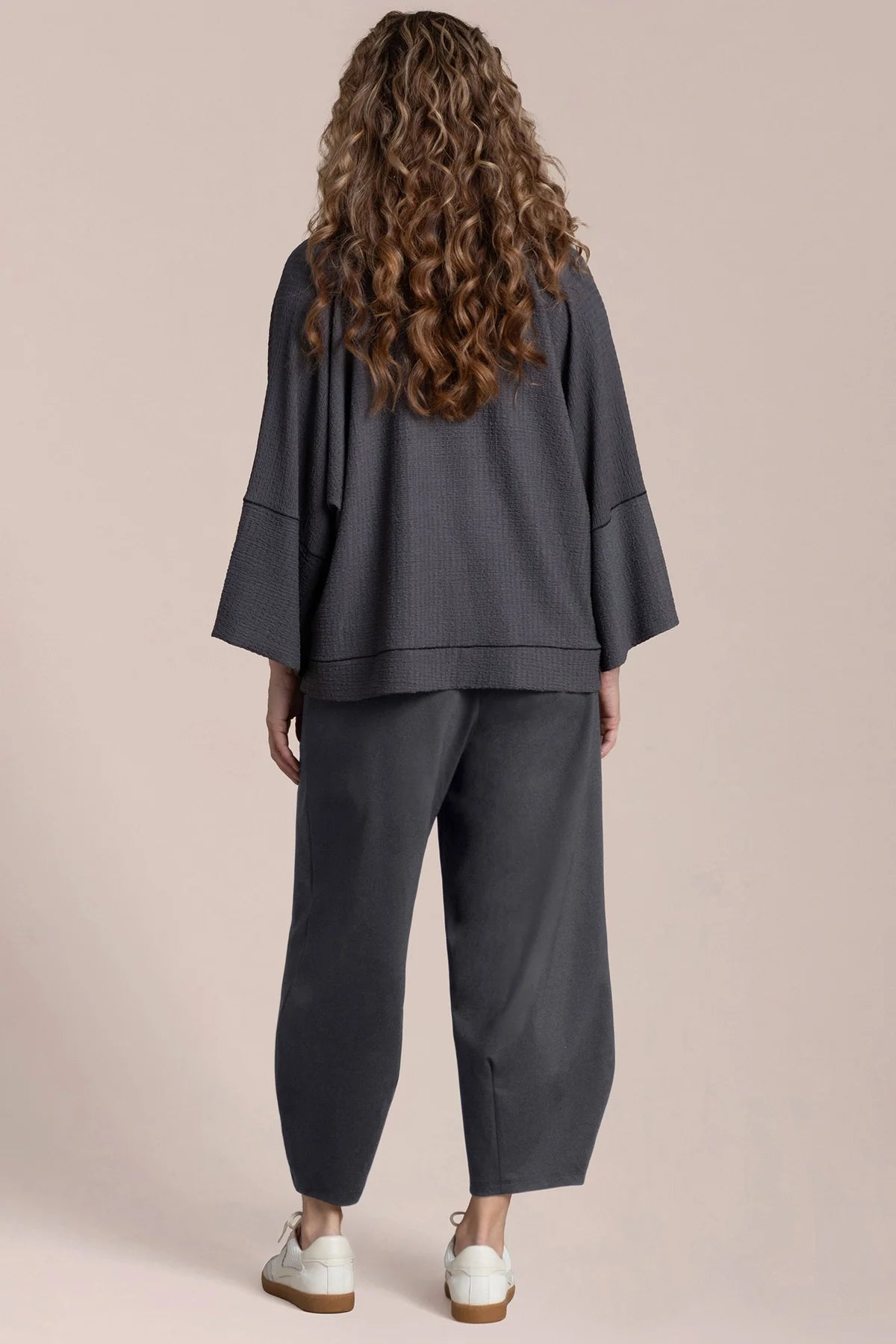 Person wearing a dark gray outfit with a matching top and pants on a beige background