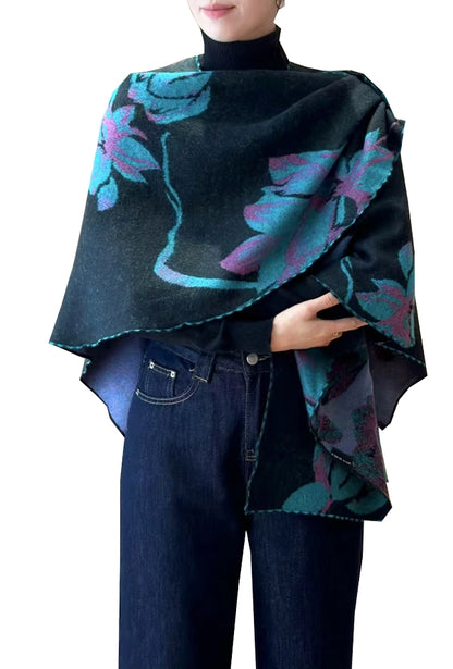 Person wearing a dark purple and green poncho with floral patterns over a black turtleneck and blue jeans on a white background.