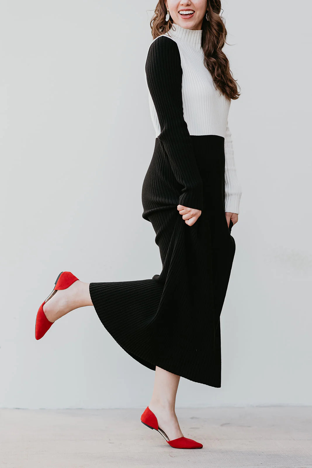 Woman wearing a black and white outfit with red shoes on a plain background