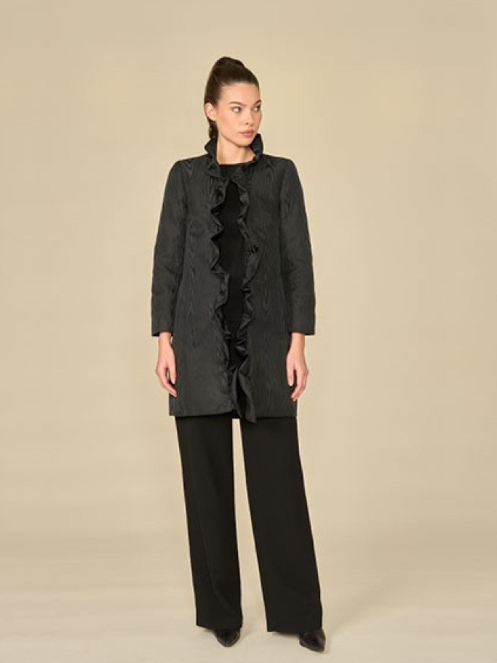 Woman wearing a black ruffled coat and pants on a beige background