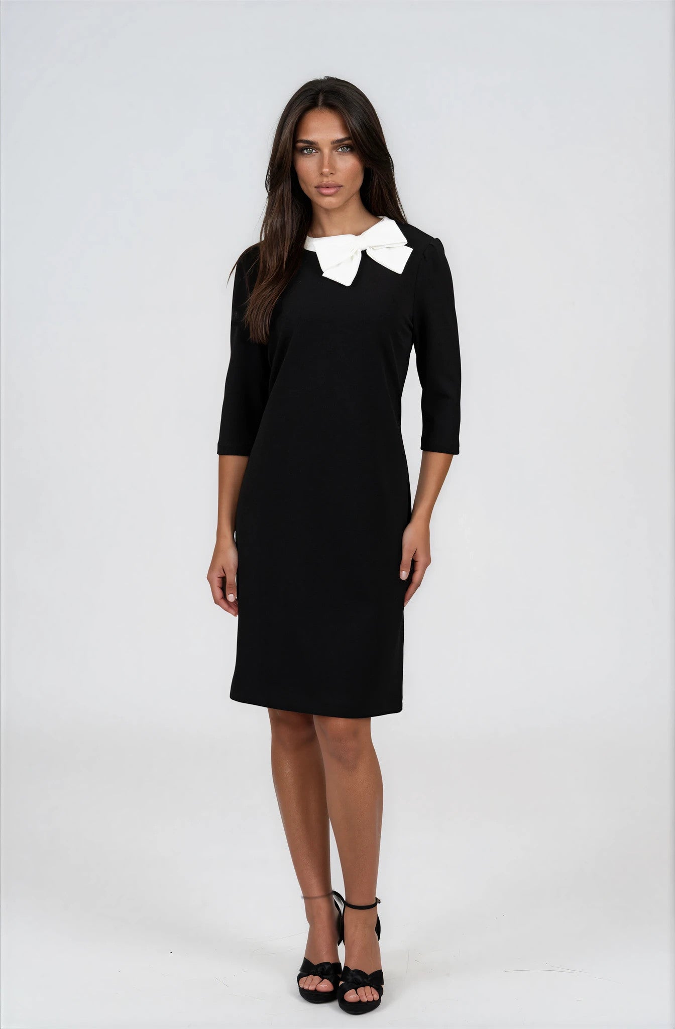 A woman modeling a black knee-length dress with three-quarter sleeves and a contrasting white bow collar