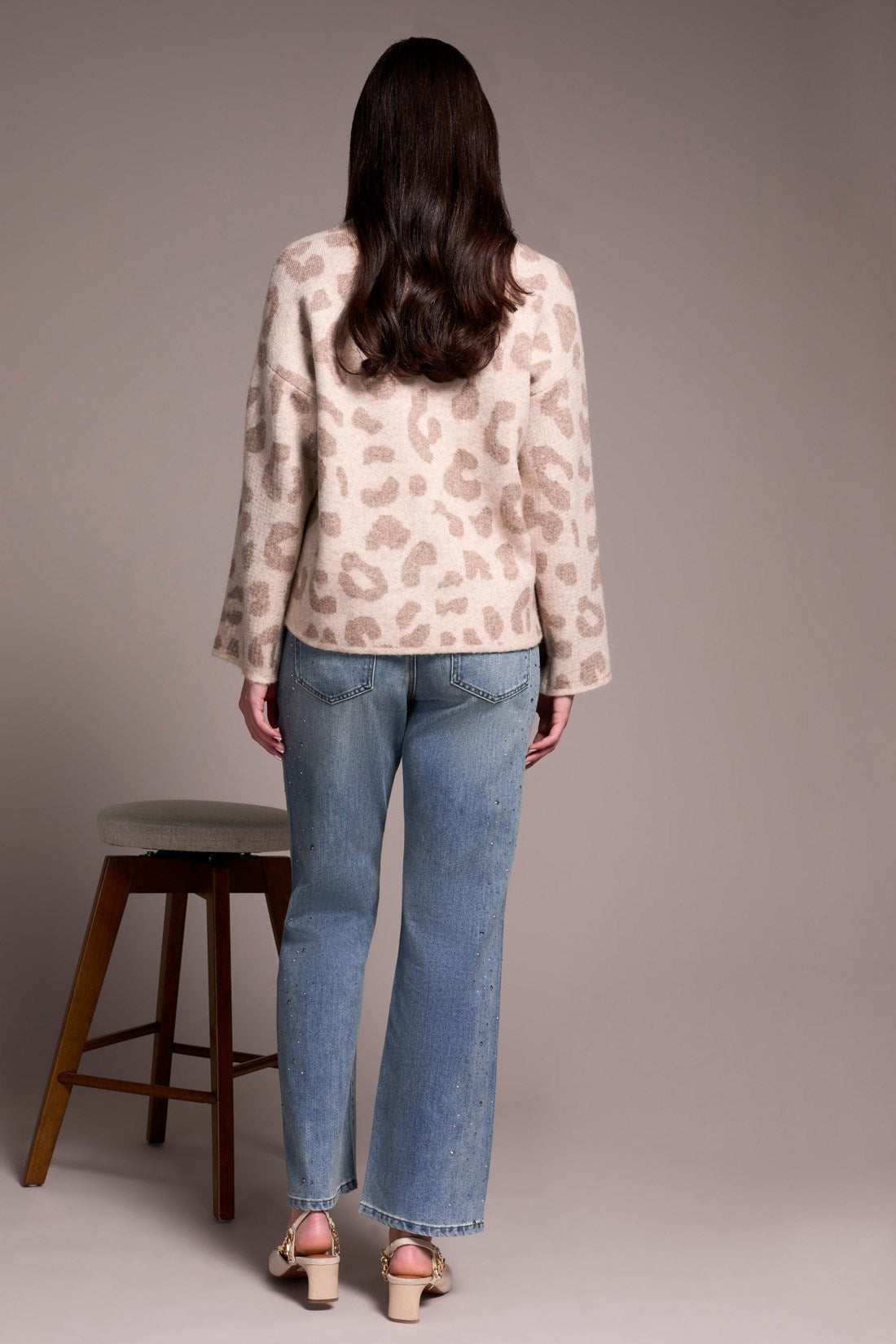 Person wearing a patterned blouse and blue jeans standing in front of a plain background