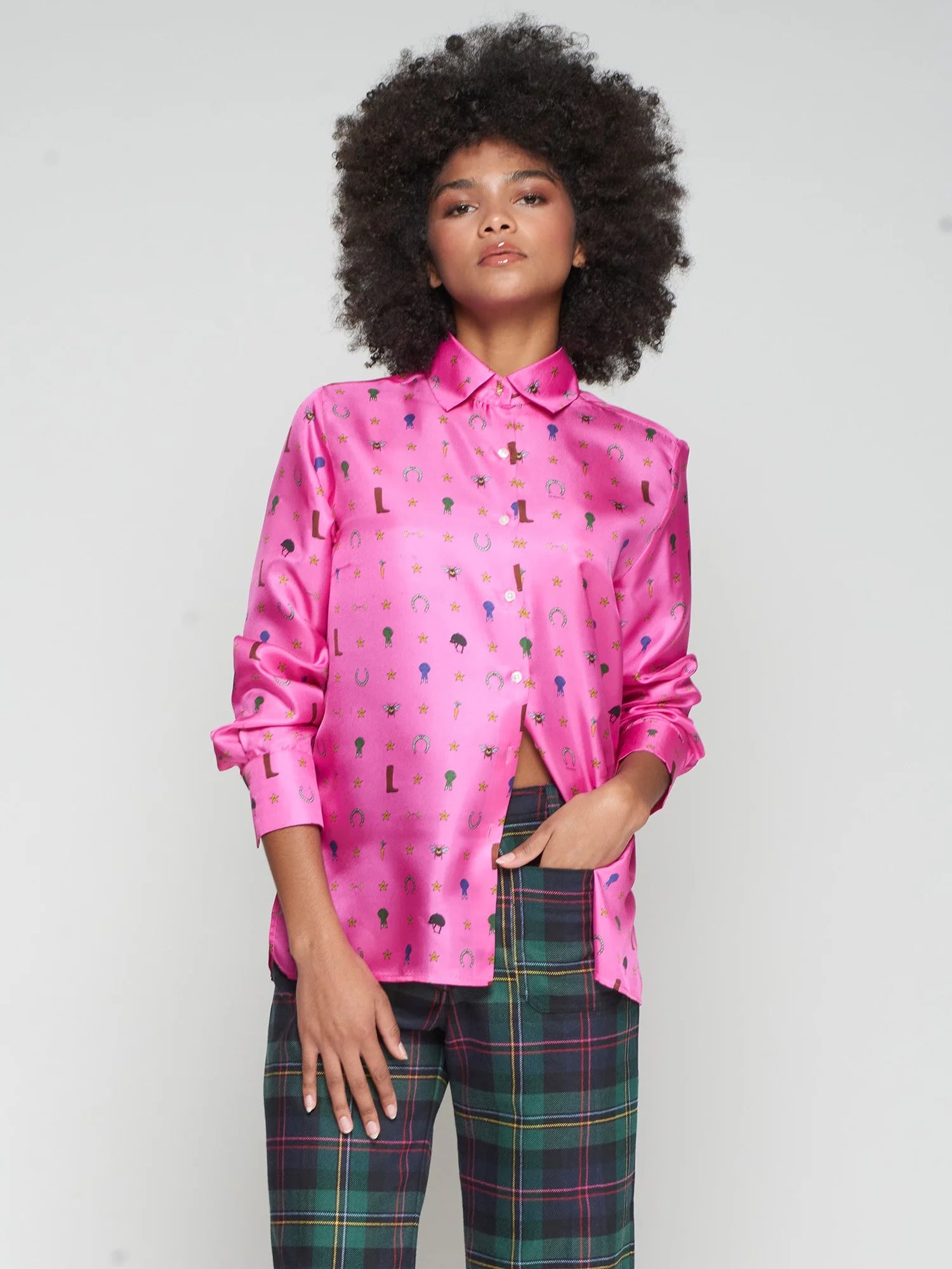 Person wearing a pink silk shirt with colorful equestrian patterns and plaid pants on a white background