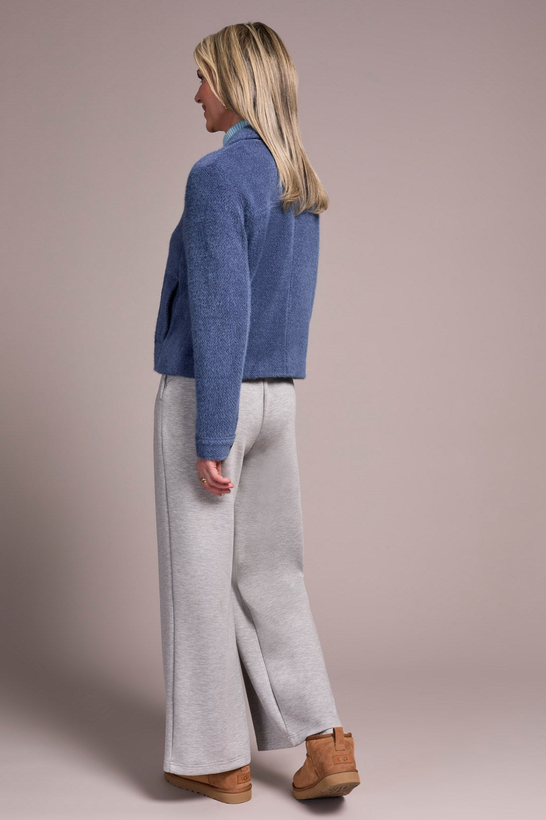 Woman wearing a blue sweater and gray pants against a beige background