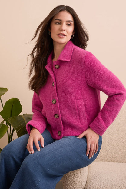 Woman wearing a bright pink cardigan sitting on a couch with a beige background