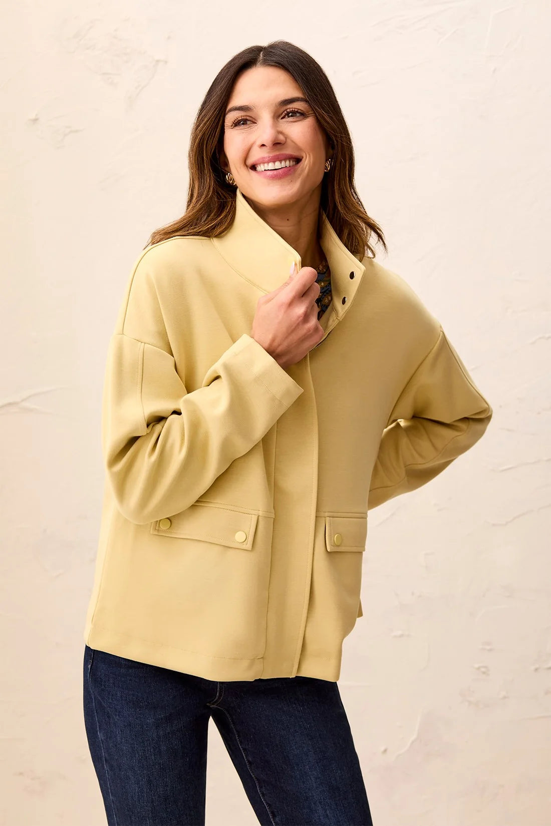 A woman wearing a light yellow jacket with a high stand collar and flap pockets by tribal Soft-Touch Zip-Up Funnel Neck Utility Jacket in the color light pear