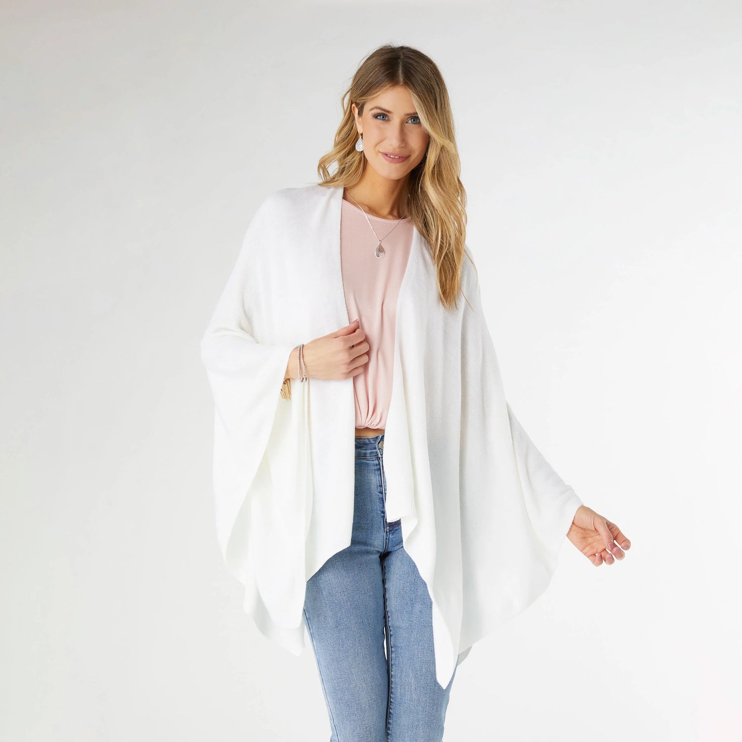 Woman wearing a white cardigan over a pink top and blue jeans on a white background